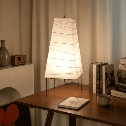 Handcrafted organic oval Washi Paper 4N Table Lamp on black tripod legs emitting a soft warm glow in a Japandi style interior setting.