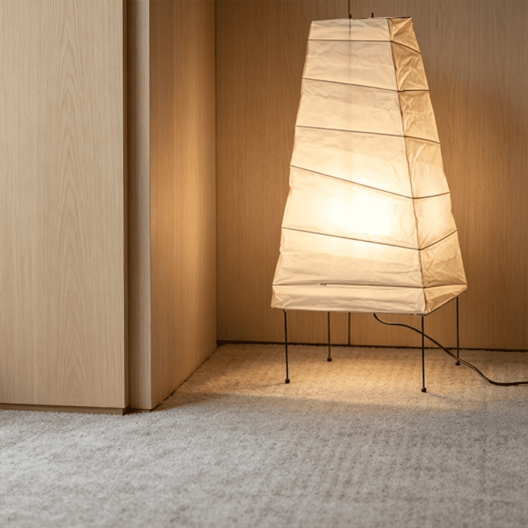 Handcrafted organic oval Washi Paper 4N Table Lamp on black tripod legs emitting a soft warm glow in a Japandi style interior setting.