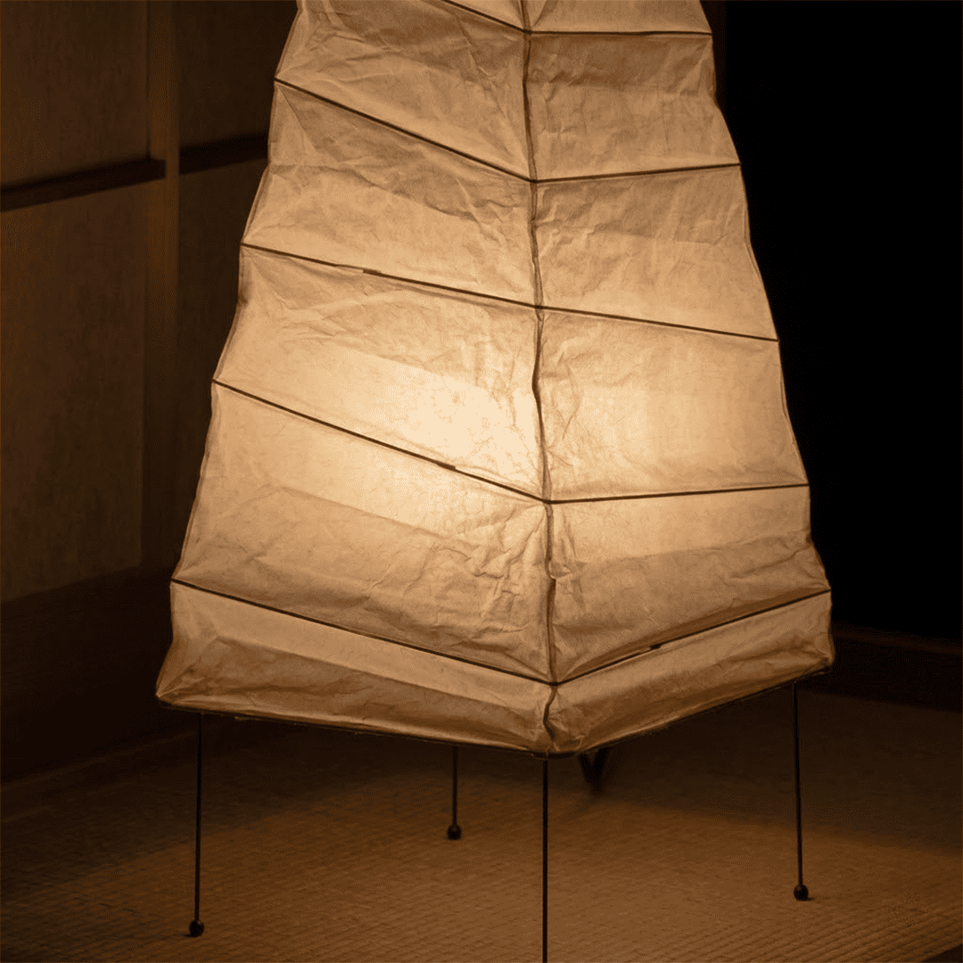 Handcrafted organic oval Washi Paper 4N Table Lamp on black tripod legs emitting a soft warm glow in a Japandi style interior setting.