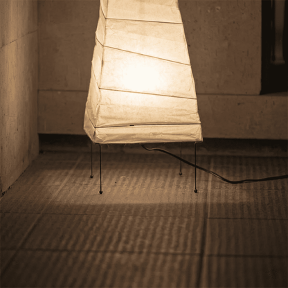 Handcrafted organic oval Washi Paper 4N Table Lamp on black tripod legs emitting a soft warm glow in a Japandi style interior setting.