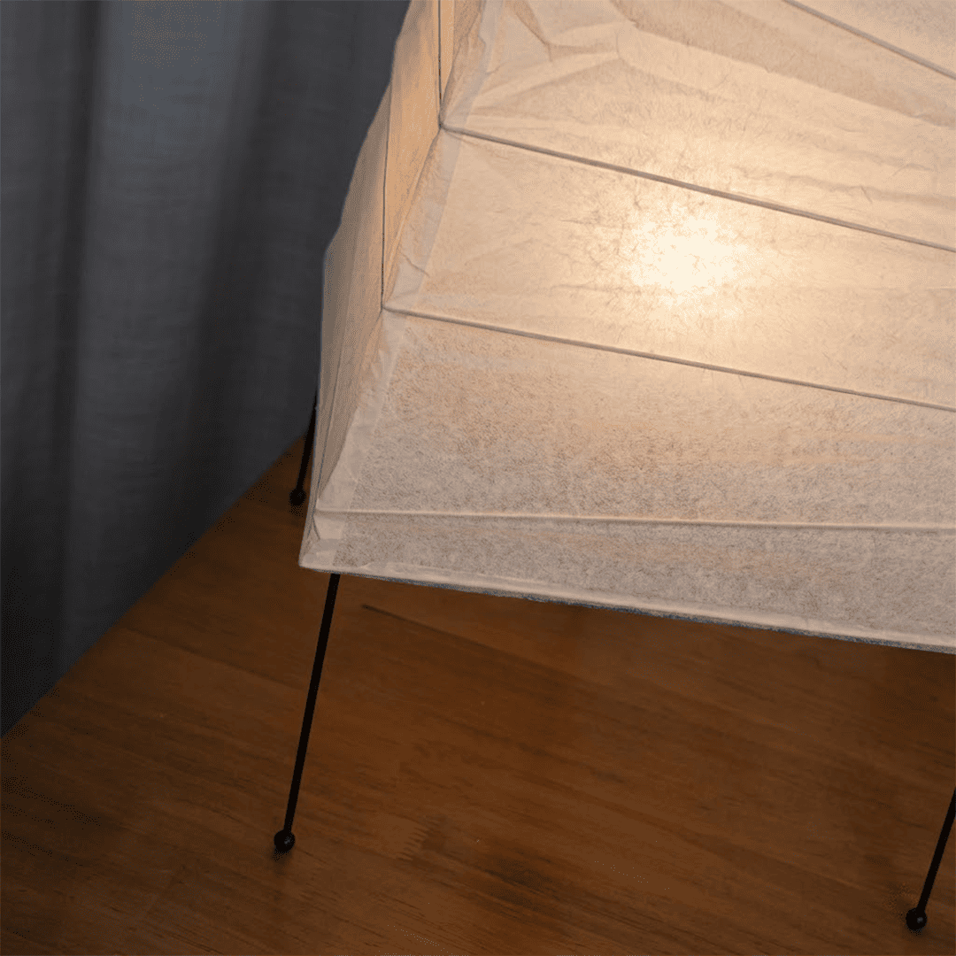 Handcrafted organic oval Washi Paper 4N Table Lamp on black tripod legs emitting a soft warm glow in a Japandi style interior setting.