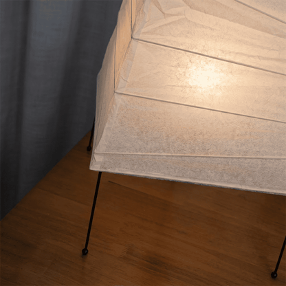 Handcrafted organic oval Washi Paper 4N Table Lamp on black tripod legs emitting a soft warm glow in a Japandi style interior setting.