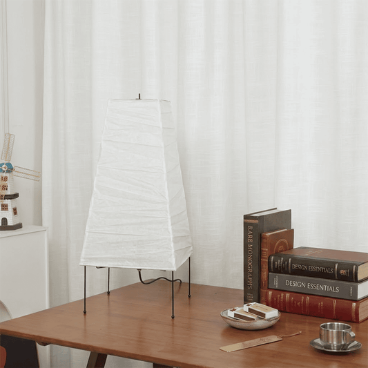 Handcrafted organic oval Washi Paper 4N Table Lamp on black tripod legs emitting a soft warm glow in a Japandi style interior setting.