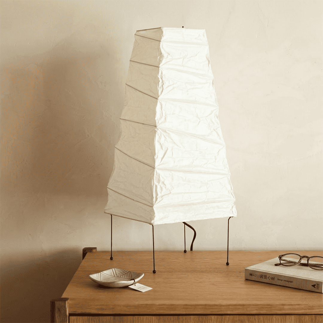 Handcrafted organic oval Washi Paper 4N Table Lamp on black tripod legs emitting a soft warm glow in a Japandi style interior setting.