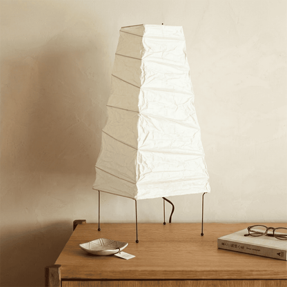 Handcrafted organic oval Washi Paper 4N Table Lamp on black tripod legs emitting a soft warm glow in a Japandi style interior setting.