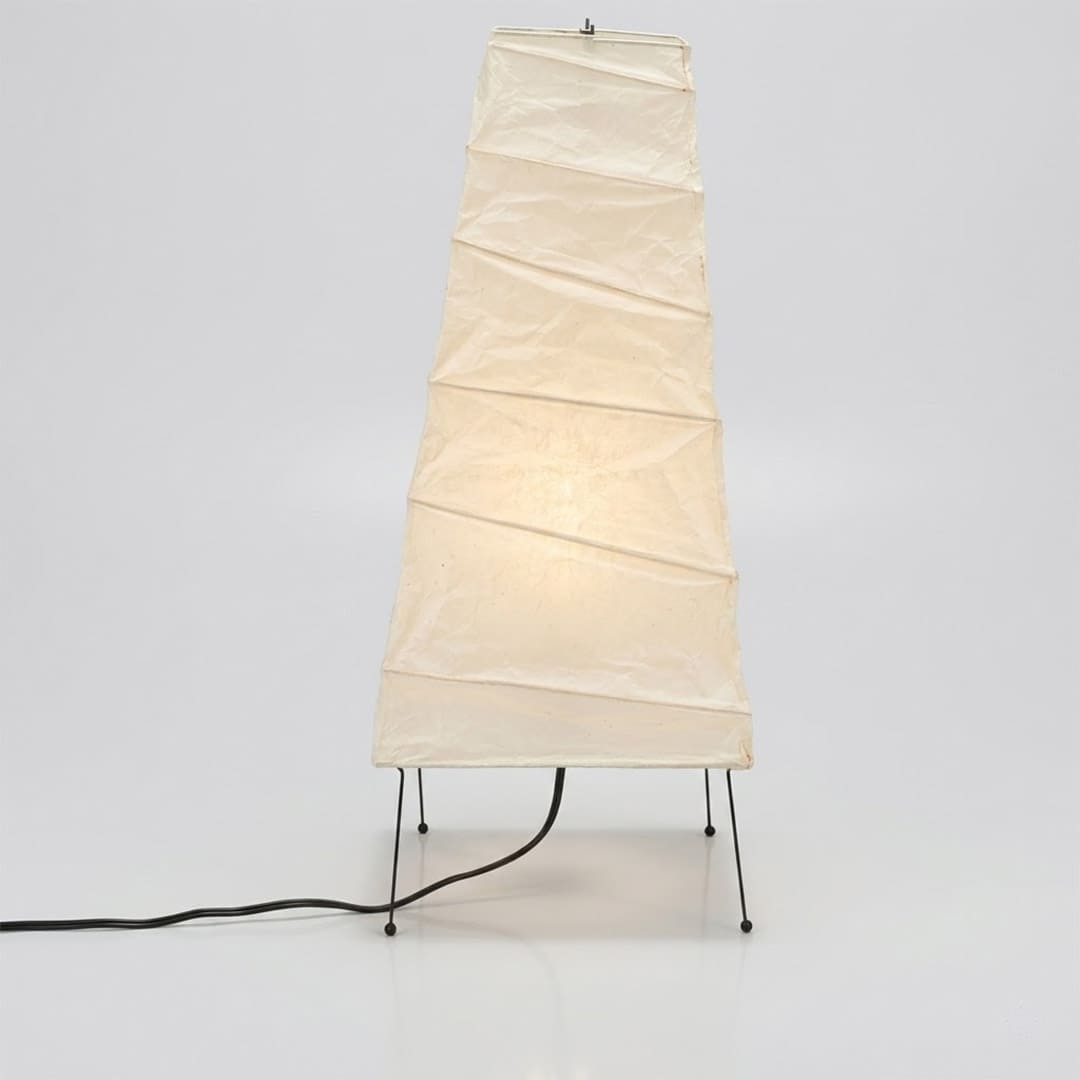 Handcrafted organic oval Washi Paper 4N Table Lamp on black tripod legs emitting a soft warm glow in a Japandi style interior setting.