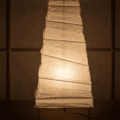 Handcrafted organic oval Washi Paper 4N Table Lamp on black tripod legs emitting a soft warm glow in a Japandi style interior setting.