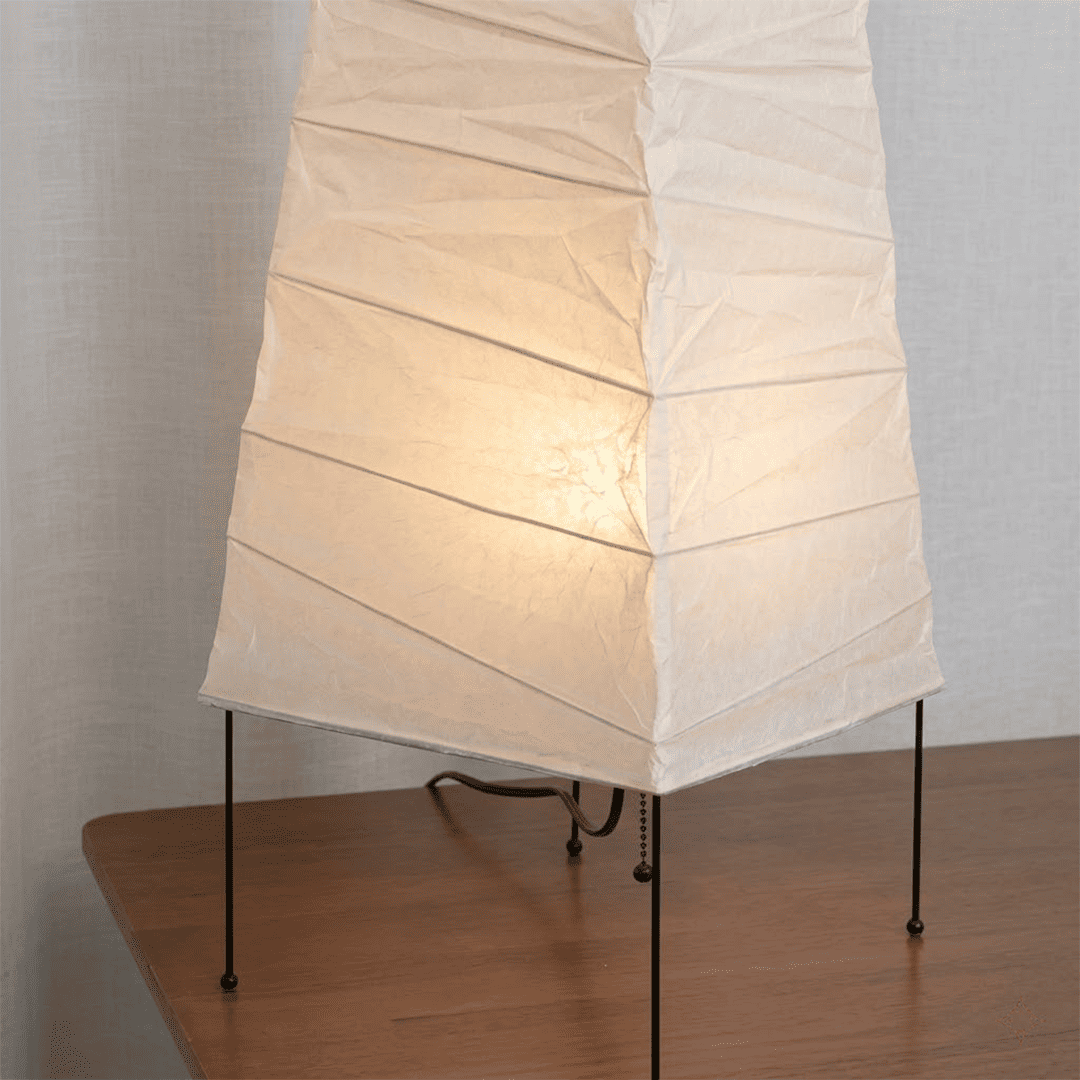 Handcrafted organic oval Washi Paper 4N Table Lamp on black tripod legs emitting a soft warm glow in a Japandi style interior setting.