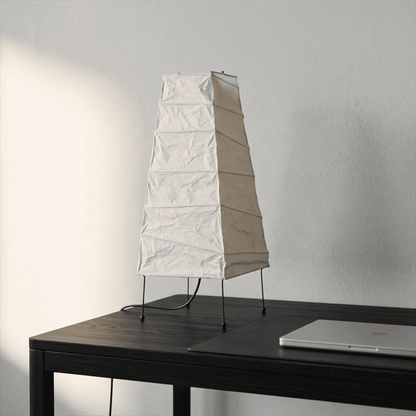 Handcrafted organic oval Washi Paper 4N Table Lamp on black tripod legs emitting a soft warm glow in a Japandi style interior setting.