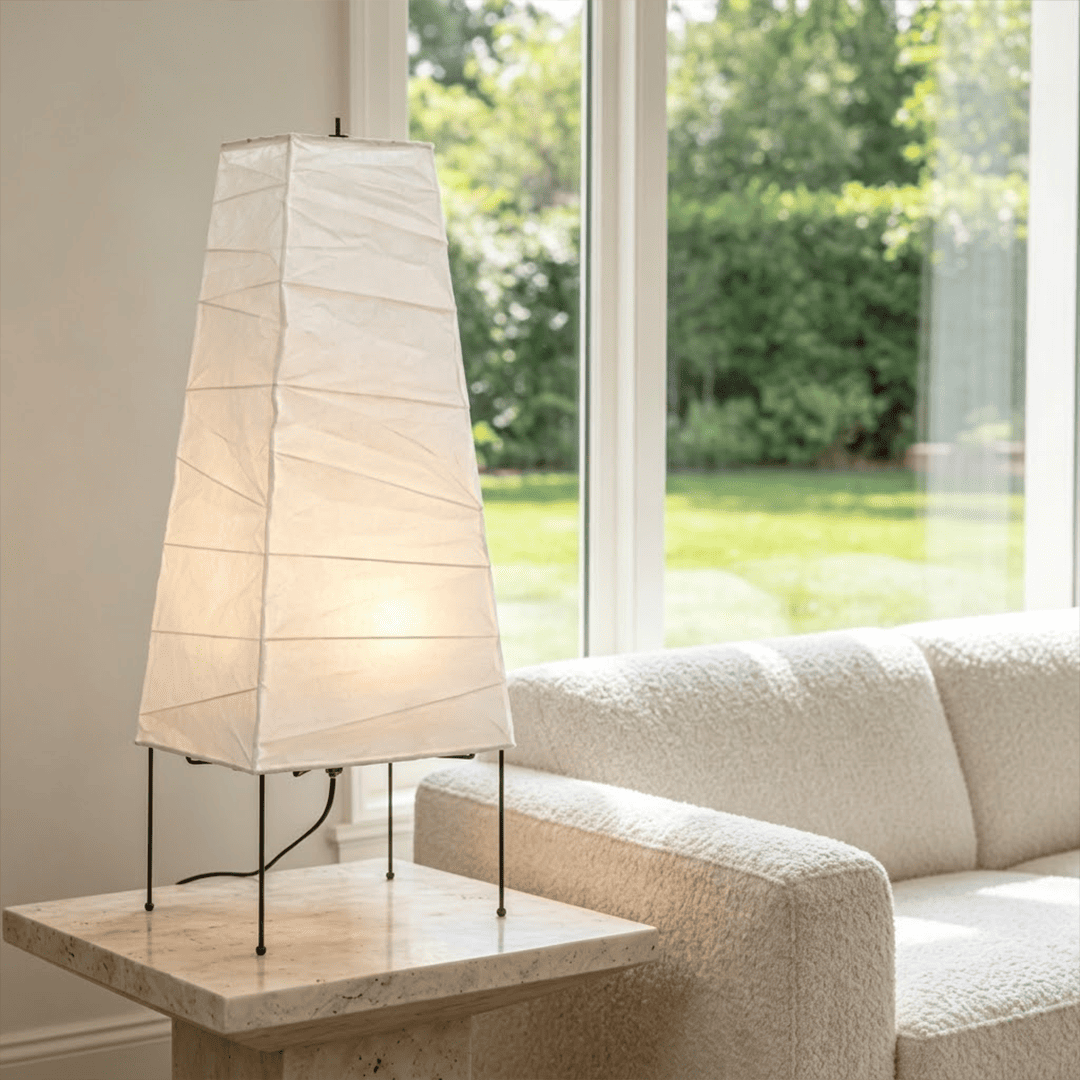 Handcrafted organic oval Washi Paper 4N Table Lamp on black tripod legs emitting a soft warm glow in a Japandi style interior setting.