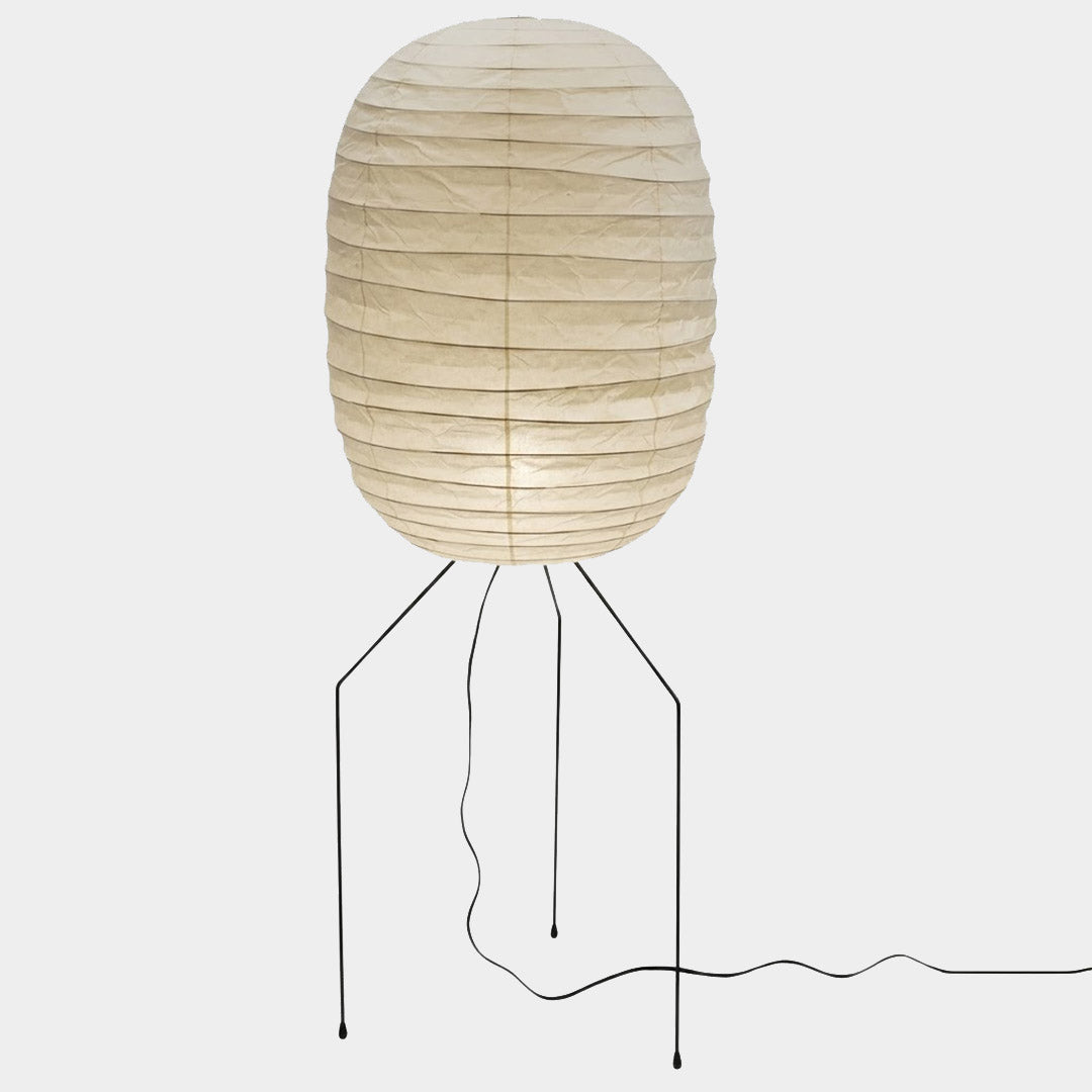 Large Akari UF3-DL floor lamp with a white washi paper shade on a black tripod metal stand, glowing with warm light in a minimalist room.