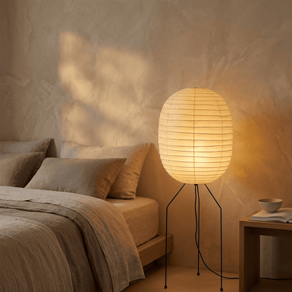 Large Akari UF3-DL floor lamp with a white washi paper shade on a black tripod metal stand, glowing with warm light in a minimalist room.