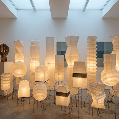 Large Akari UF3-DL floor lamp with a white washi paper shade on a black tripod metal stand, glowing with warm light in a minimalist room.