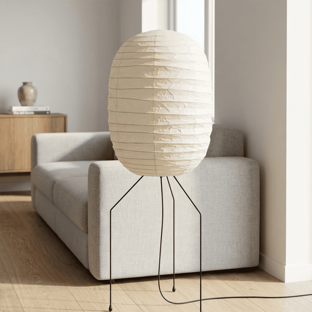 Large Akari UF3-DL floor lamp with a white washi paper shade on a black tripod metal stand, glowing with warm light in a minimalist room.