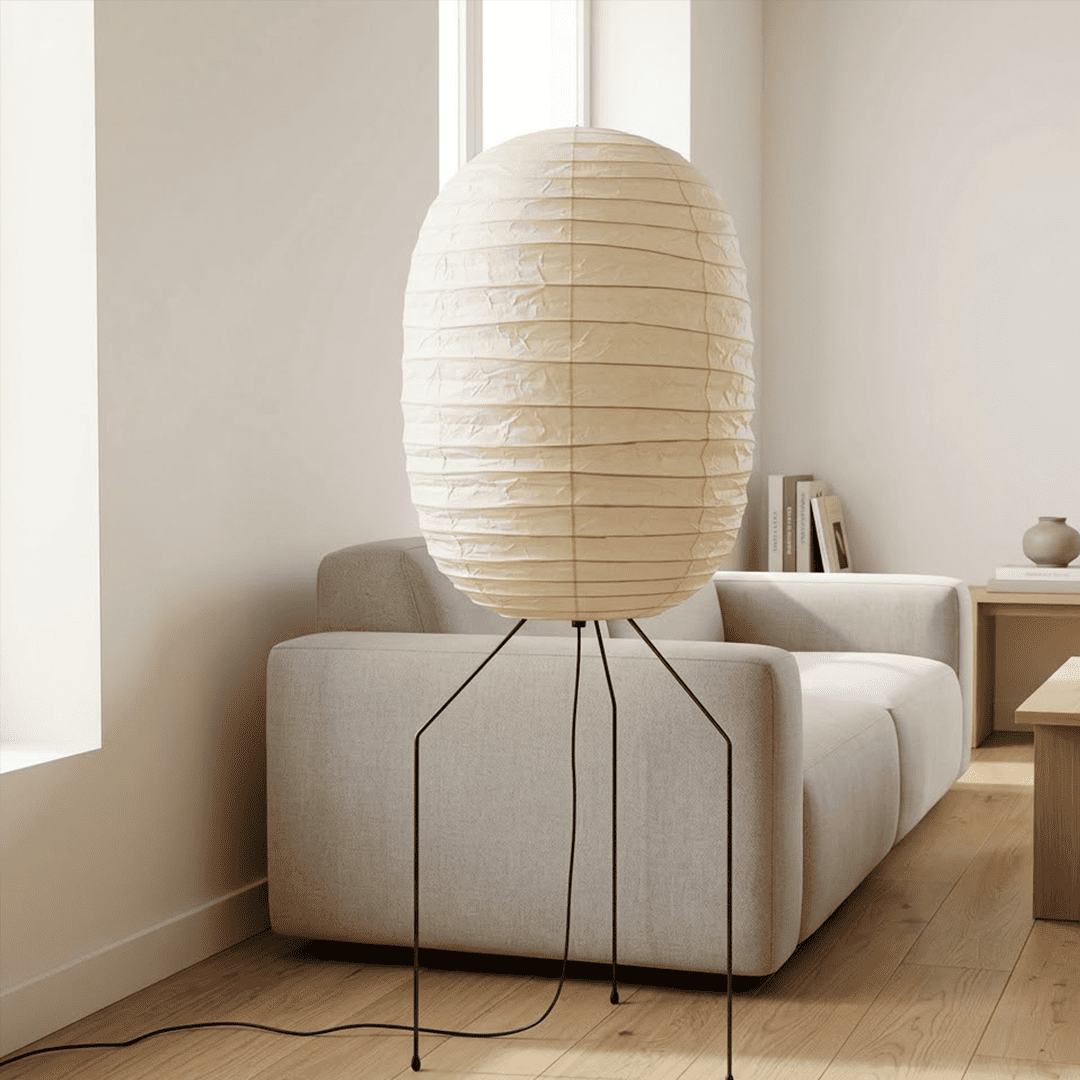 Large Akari UF3-DL floor lamp with a white washi paper shade on a black tripod metal stand, glowing with warm light in a minimalist room.