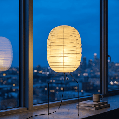 Large Akari UF3-DL floor lamp with a white washi paper shade on a black tripod metal stand, glowing with warm light in a minimalist room.