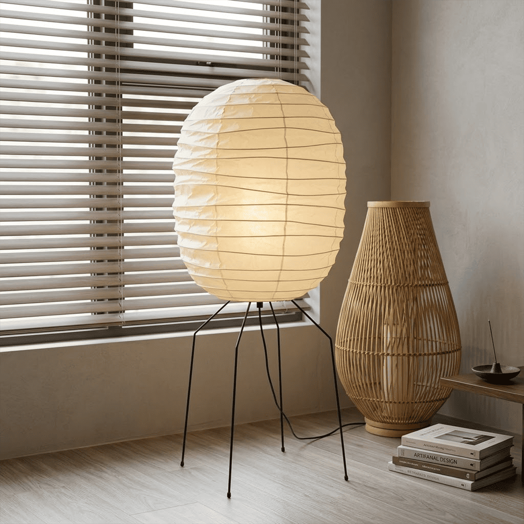 Large Akari UF3-DL floor lamp with a white washi paper shade on a black tripod metal stand, glowing with warm light in a minimalist room.