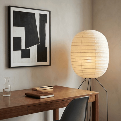 Large Akari UF3-DL floor lamp with a white washi paper shade on a black tripod metal stand, glowing with warm light in a minimalist room.