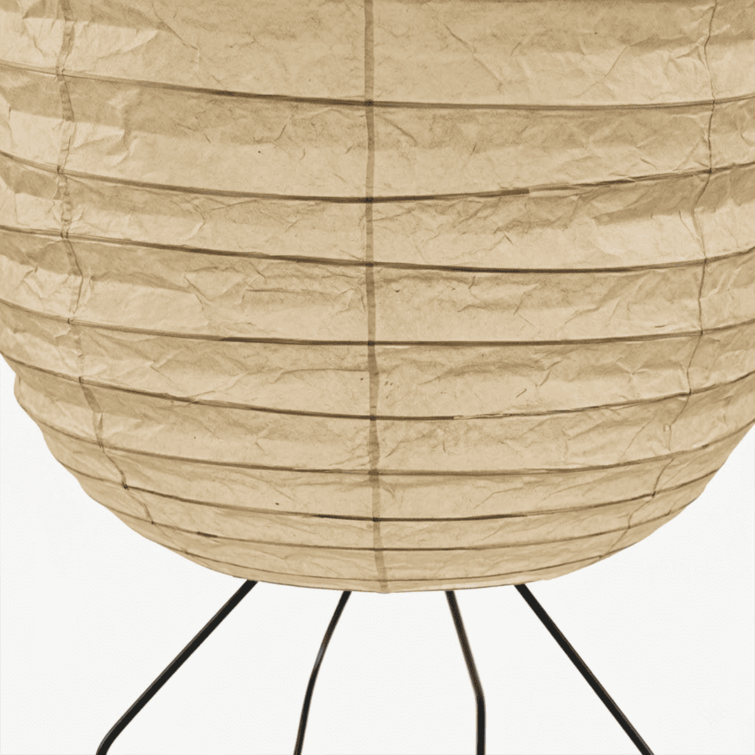 Large Akari UF3-DL floor lamp with a white washi paper shade on a black tripod metal stand, glowing with warm light in a minimalist room.