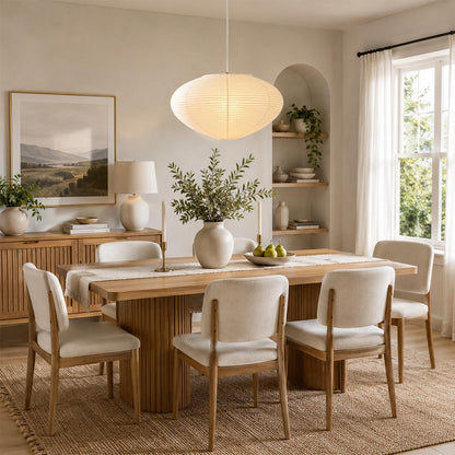 Stuber Lighting Japanese rice paper pendant light illuminated over a wooden dining table, organic modern Japandi dining room decor with minimalist oval lantern hanging lamp.