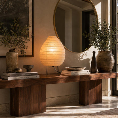 Japanese style Akari 22N Lantern Table Lamp placed on a rustic wooden credenza beneath a round wall mirror by Stuber Lighting.