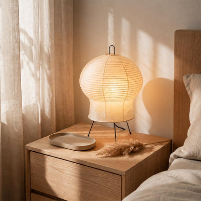 Akari 2N Table Lamp casting warm light on a wooden bedside nightstand in a minimalist bedroom by Stuber Lighting