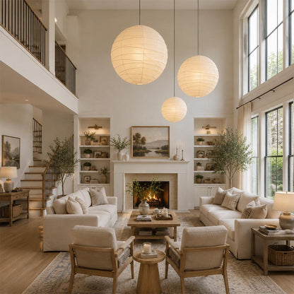 A cluster of three round Washi paper pendant lights in varying sizes, hanging at staggered heights in a warm, luxury high-ceiling living room with neutral sofas and a fireplace