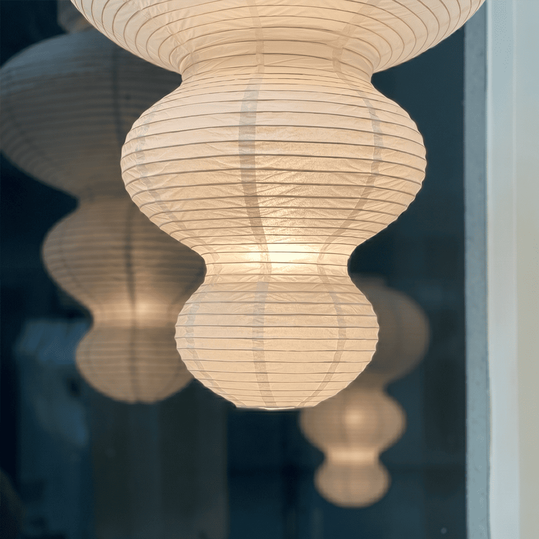Large Akari Juni washi paper pendant lamp glowing in a minimalist Japandi living room with warm 3000K light.