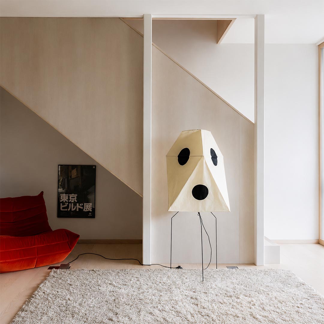 Sculptural geometric paper floor lamp under a staircase in a modern minimalist home.