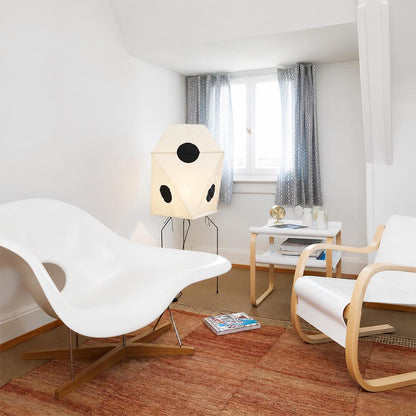 Mid-century modern origami floor lamp in a bright living room with white accent chairs and red rug.
