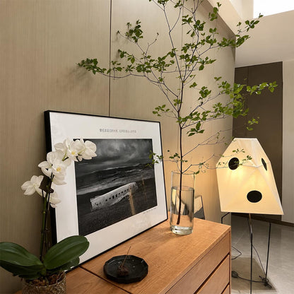 Modernist paper shade floor lamp glowing beside a wooden sideboard and framed wall art.