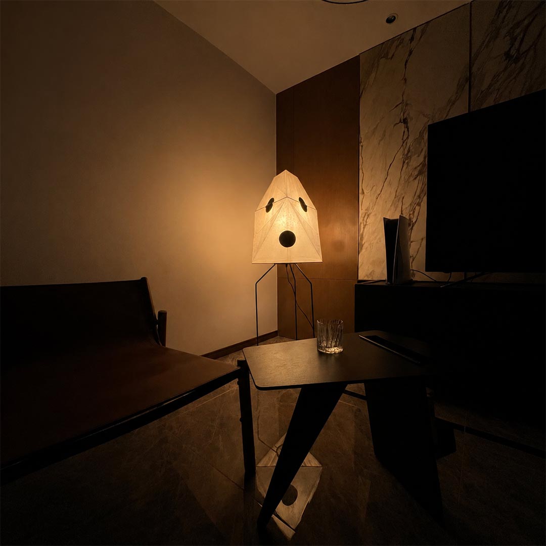 Paper lantern floor lamp emitting soft ambient warm glow in a dark minimalist living room.