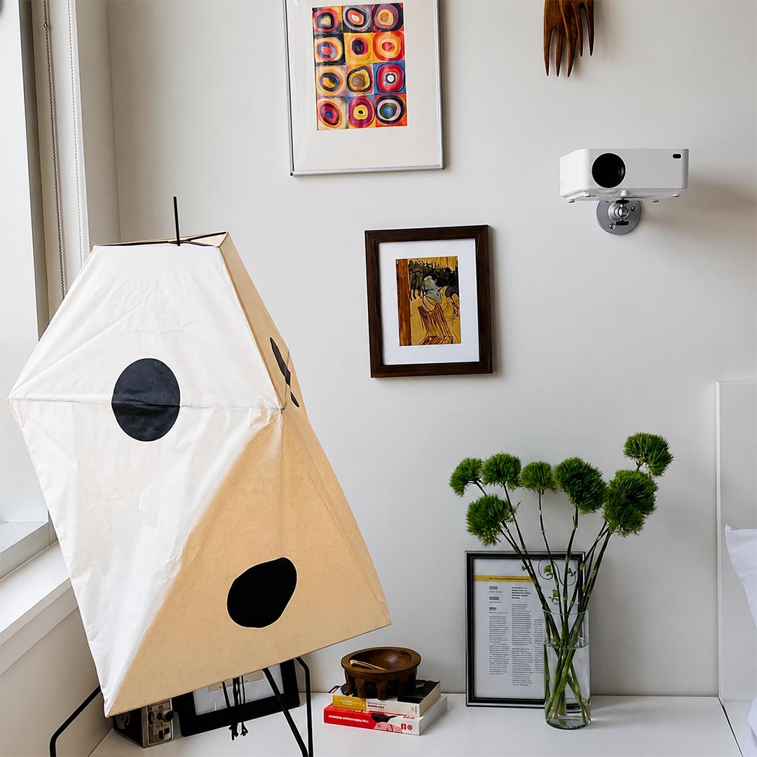Close-up of geometric paper shade floor lamp next to framed gallery art and green plants.