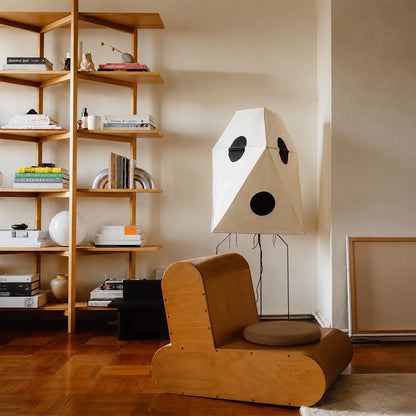 Wabi-Sabi paper floor lamp glowing beside a cardboard armchair and tall wooden shelving.