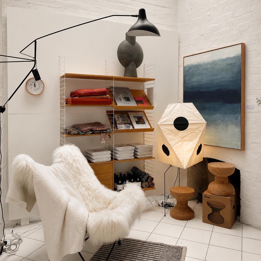 Wabi-Sabi paper floor lamp illuminated next to a plush lounge chair and wooden shelving in a cozy room.