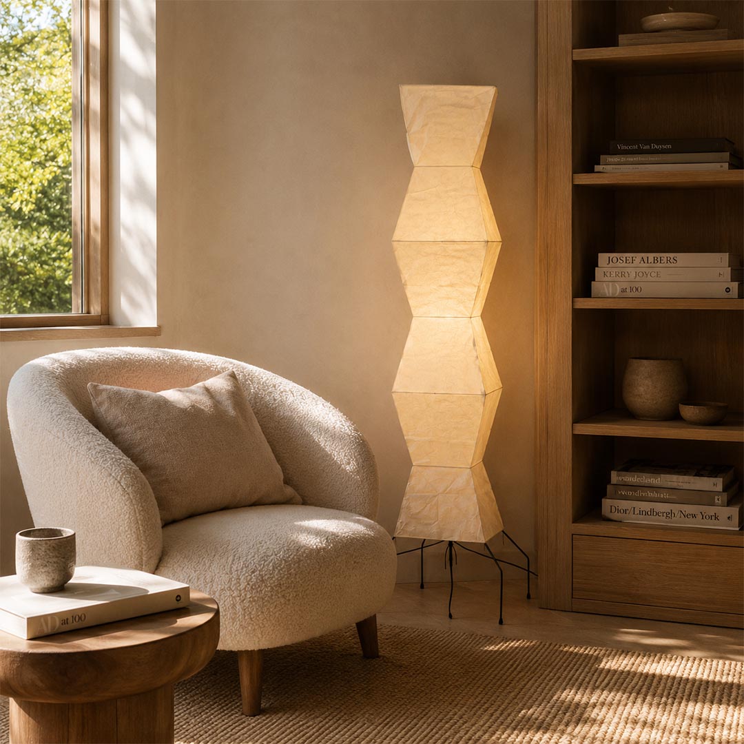 Sunlit Japandi room corner showcasing a glowing Akari UF4-L9 Floor Lamp near a plush lounge chair by Stuber Lighting.