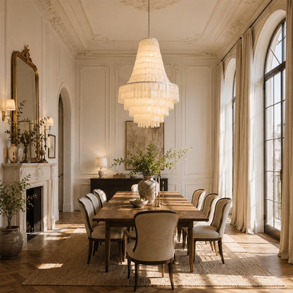 Capiz shell tiered chandelier hanging over a long wooden dining table with upholstered chairs in a sunny room.