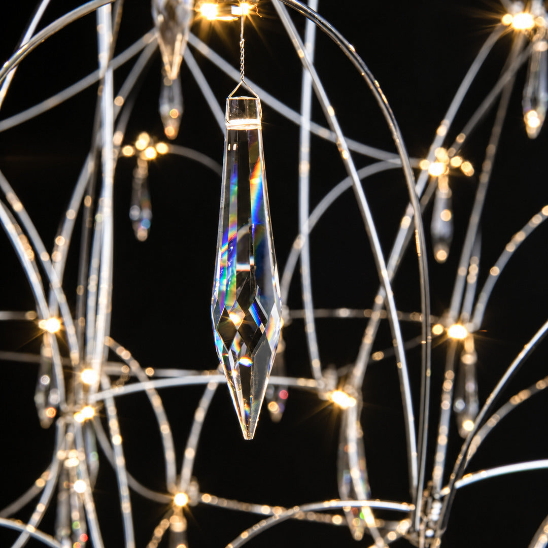 Warm light refracting through the teardrop crystals of the Astra chandelier scattering glints on the walls