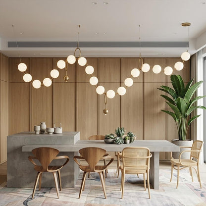 Cascadia horizontal chandelier above long dining table pearl globes warm glow elegant interior
