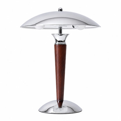 Casco wood table lamp with a polished chrome dome shade on a solid walnut stem glowing warm on a desk
