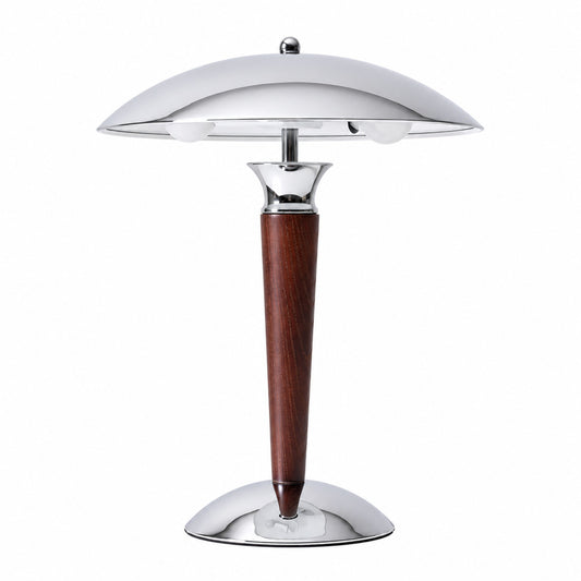 Casco wood table lamp with a polished chrome dome shade on a solid walnut stem glowing warm on a desk