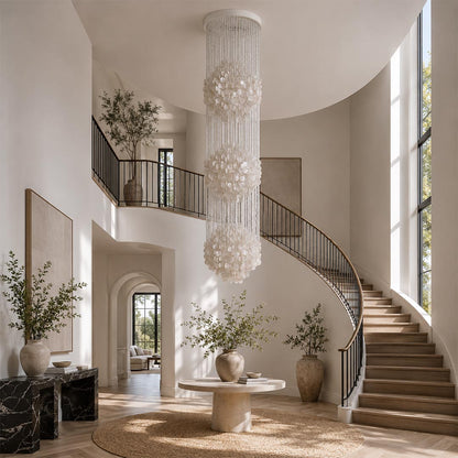 Coralia FUN tall style staircase shell chandelier hanging in a grand villa foyer next to a curved staircase.