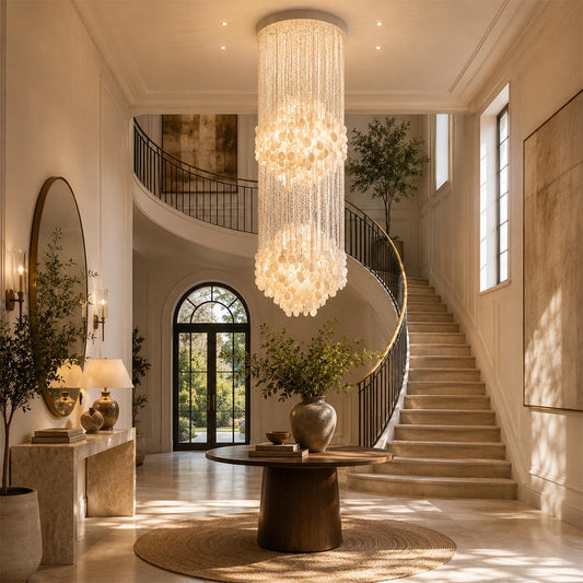 Coralia FUN tall staircase shell chandelier hanging over a round entryway table near a grand curved stairwell.