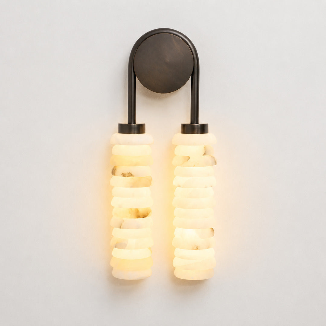 Warm integrated LED glow diffusing through the ribbed alabaster columns of the Duetto wall sconce