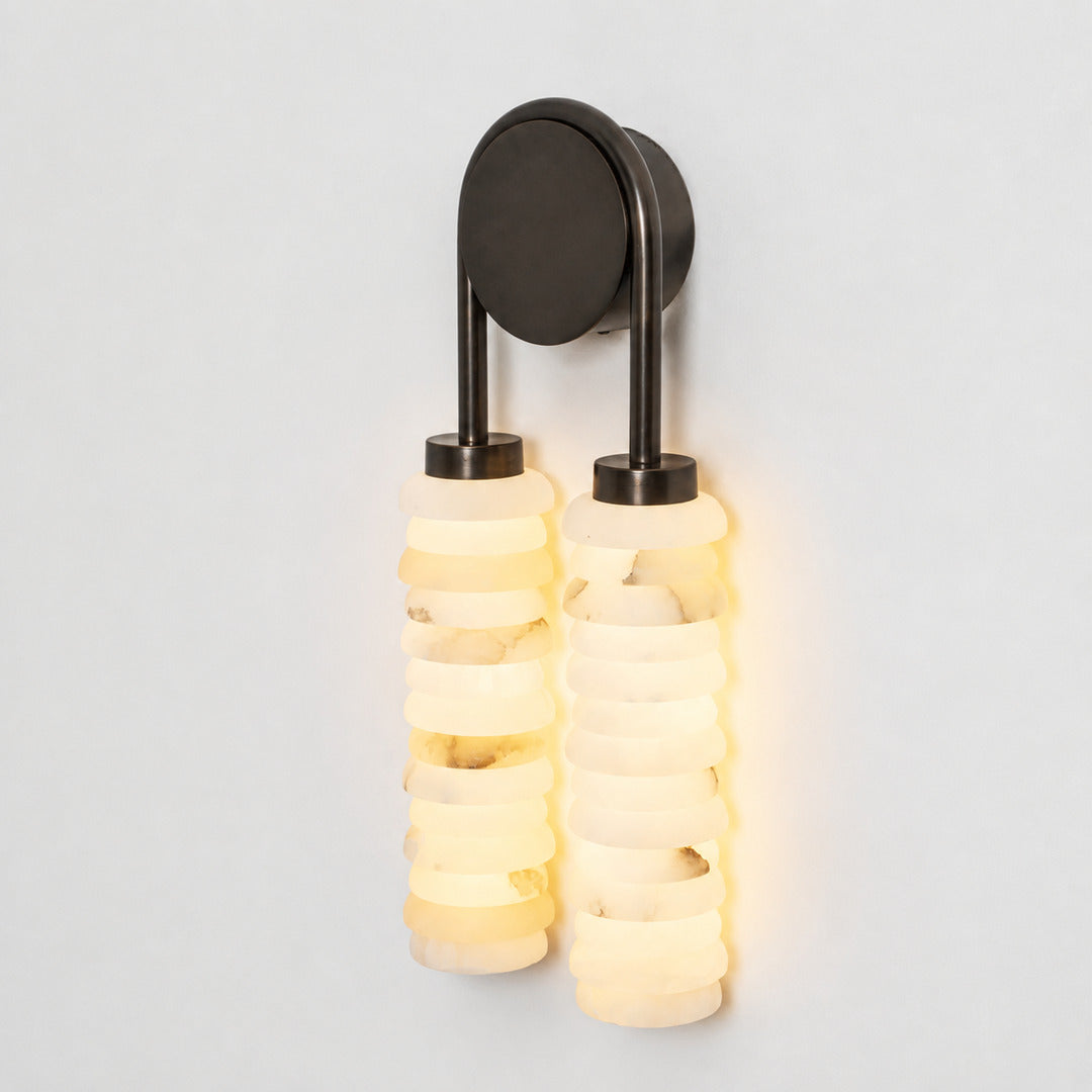 Warm integrated LED glow diffusing through the ribbed alabaster columns of the Duetto wall sconce