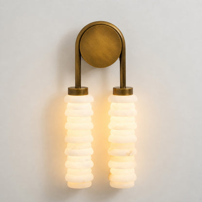 Warm integrated LED glow diffusing through the ribbed alabaster columns of the Duetto wall sconce