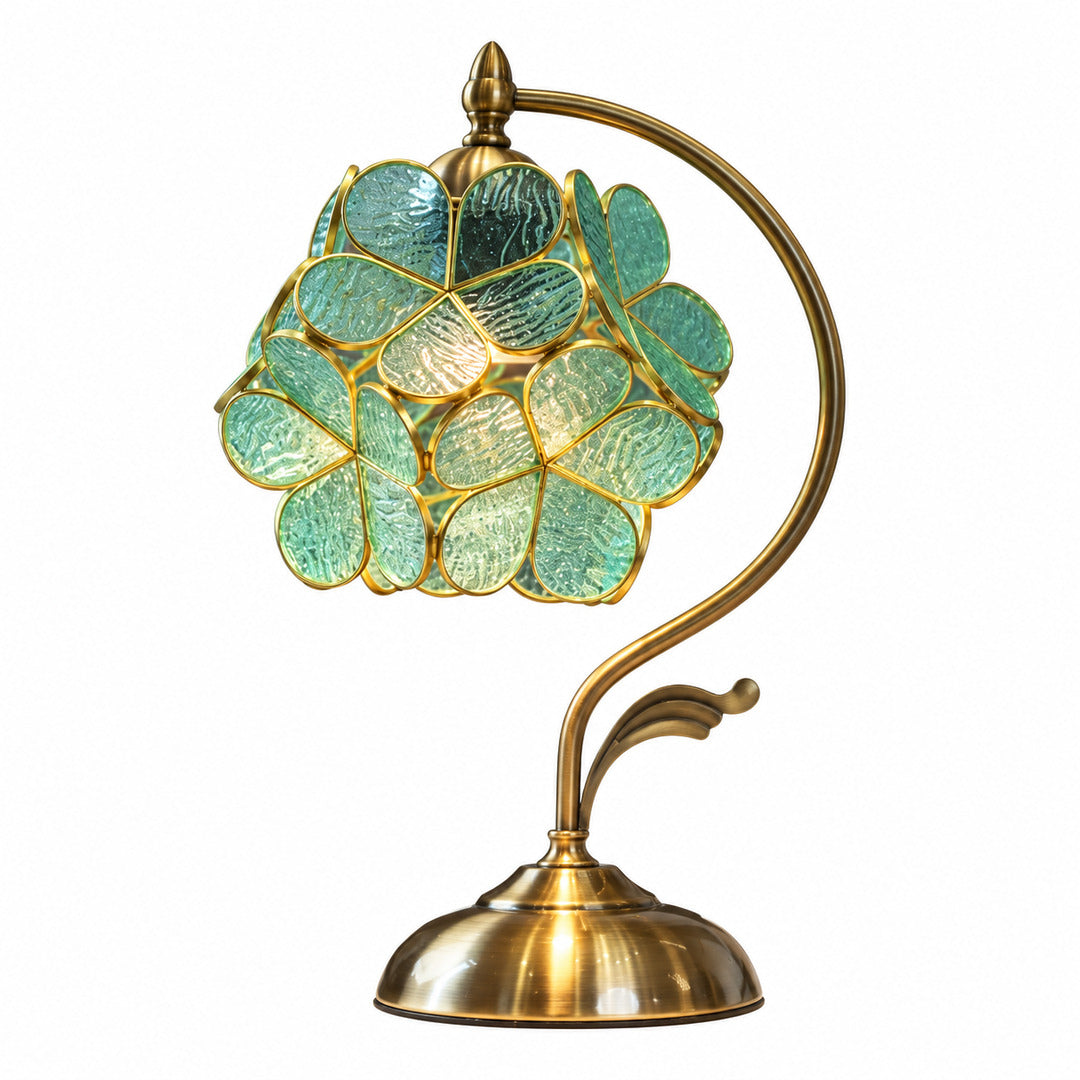 Foglia glass table lamp with a cluster of green glass leaves on a curved brass arm glowing warm on a desk