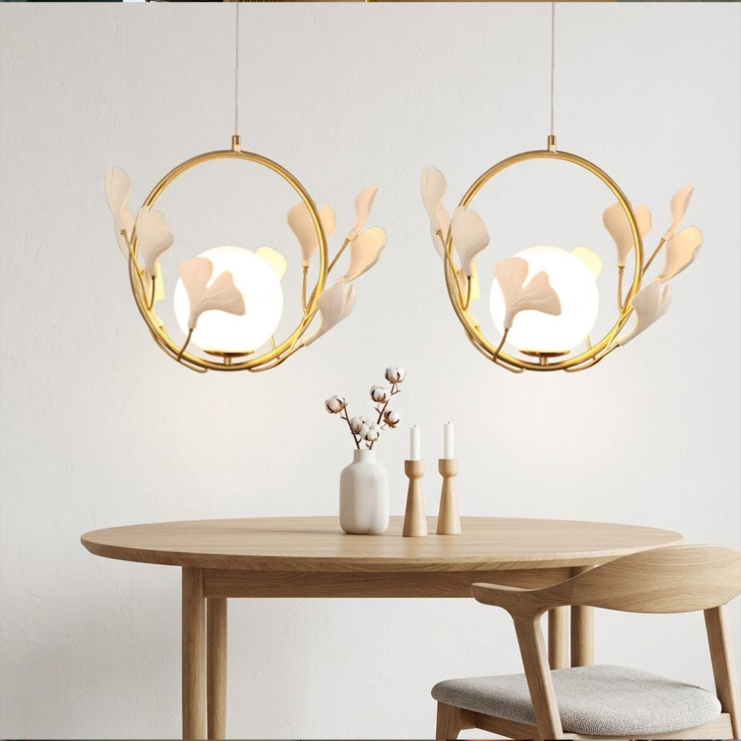 Ginkgo botanical pendant hanging above oval dining table Japandi interior warm glow porcelain leaves brass halo