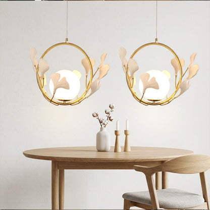 Ginkgo botanical pendant hanging above oval dining table Japandi interior warm glow porcelain leaves brass halo