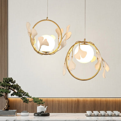 Ginkgo botanical pendant hanging above oval dining table Japandi interior warm glow porcelain leaves brass halo